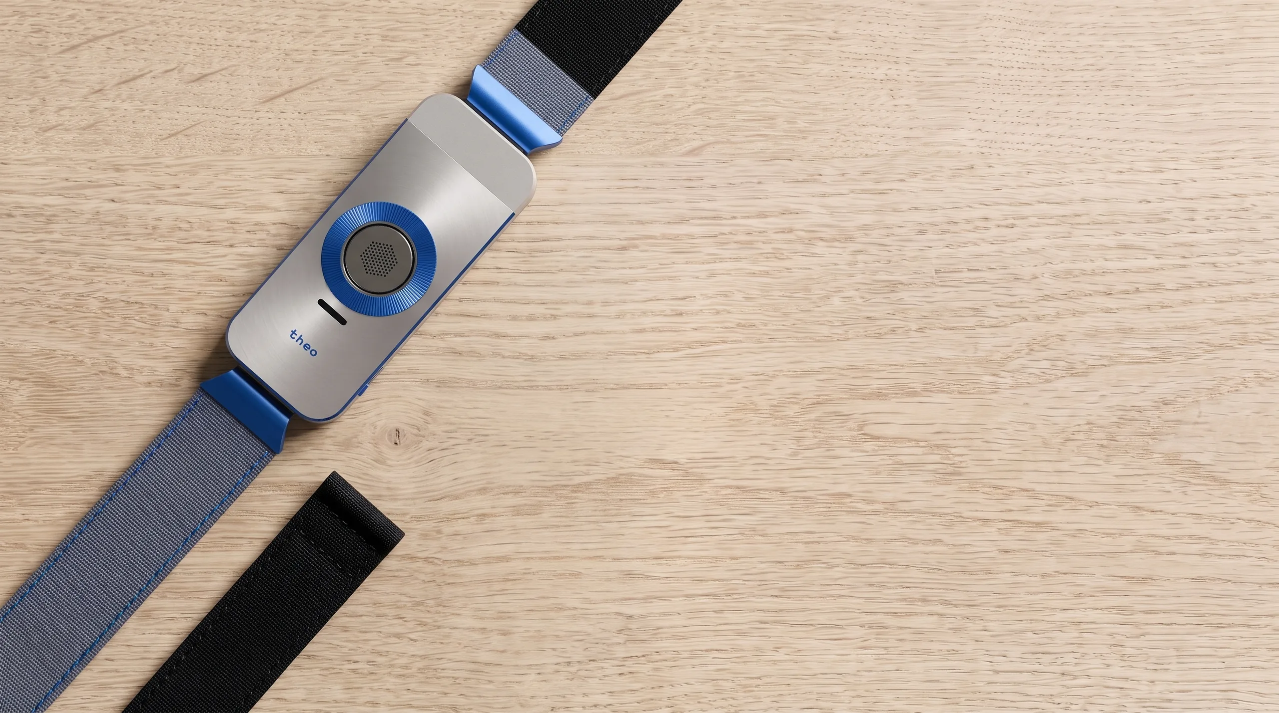 The Nickel / Cobalt case on a pale oak table with a second strap laid beside it.