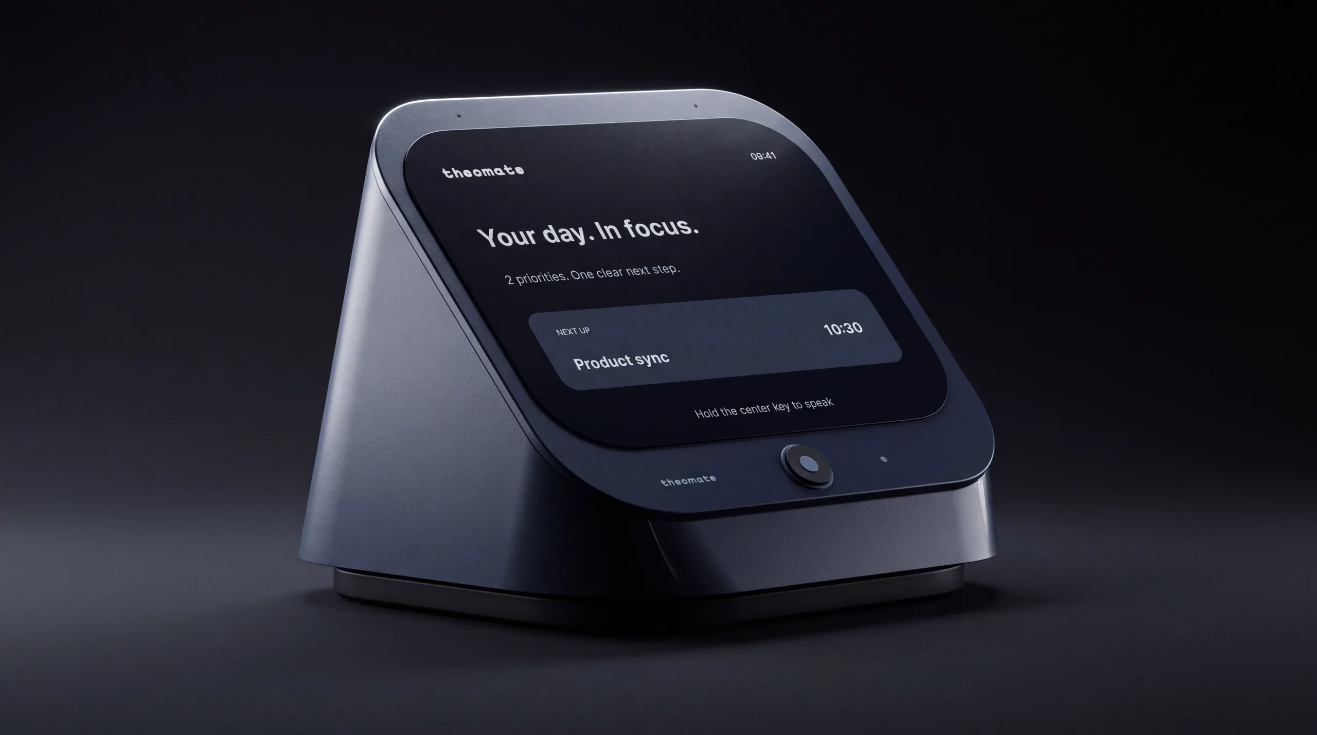 The TheoMate Desk in the Midnight finish alone on a dark graphite field, a single light raking the soft radius of its shell, its tilted face showing the day in focus above the round centre key.